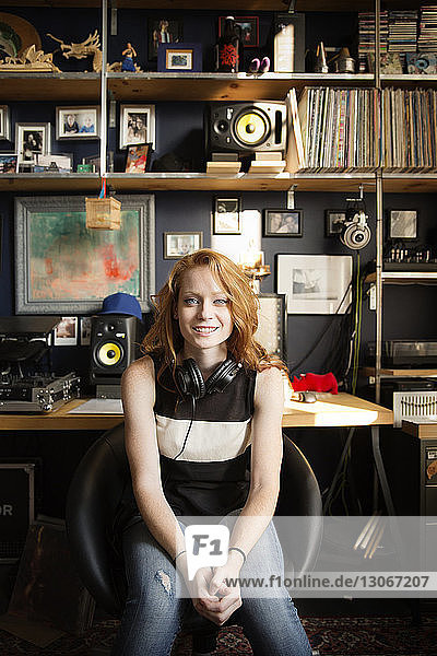 Portrait of happy female DJ sitting at sound recording studio