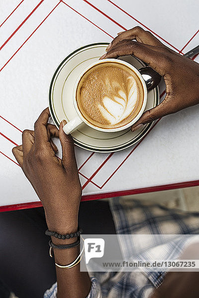Ausschnitt einer Frau mit Cappuccino in der Hand  während sie im Straßencafé sitzt
