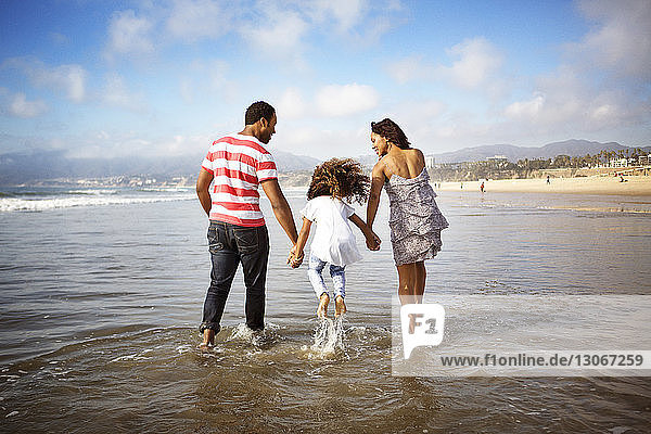 Girl jumping while walking with parents in water at beach