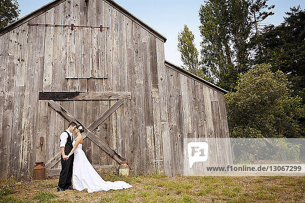 Newlywed couple standing on grassy field against house