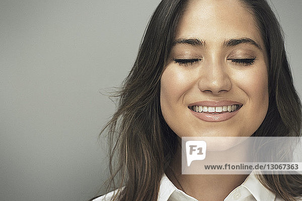 Smiling woman with eyes closed against gray background