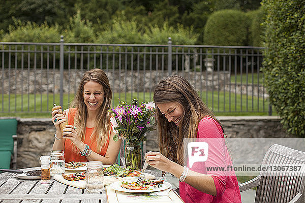 Glückliche Freunde essen  während sie auf dem Rasen am Tisch sitzen