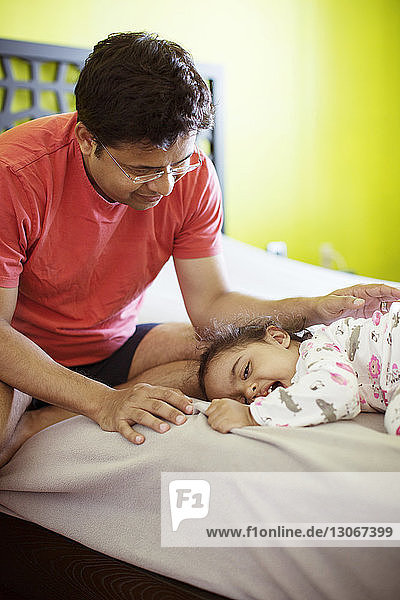 Happy father playing with daughter while sitting on bed at home