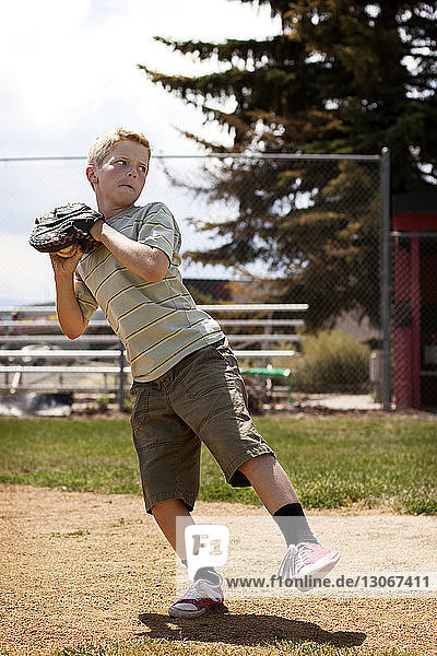 Boy throwing ball while standing at base ball field