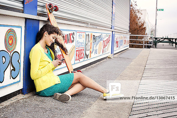 Seitenansicht einer Teenagerin  die ein Smartphone benutzt  während sie vor geschlossenen Lebensmittelgeschäften sitzt