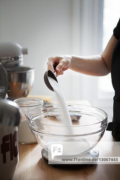 Ausgeschnittenes Bild einer Frau  die Mehl in eine Schüssel gießt  die im Küchenmaßstab gehalten wird