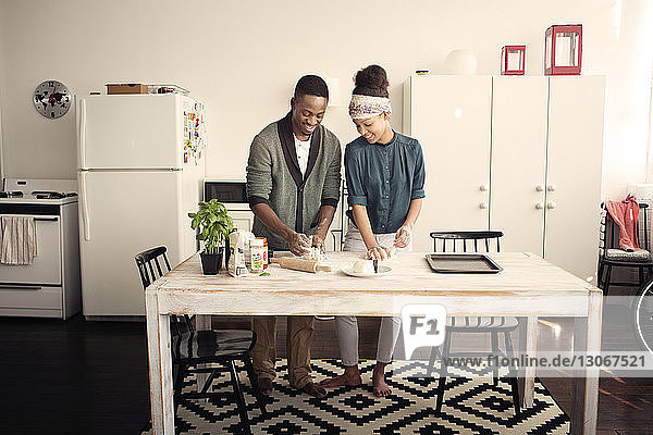 Lächelndes Paar knetet Teig bei Tisch in der Küche