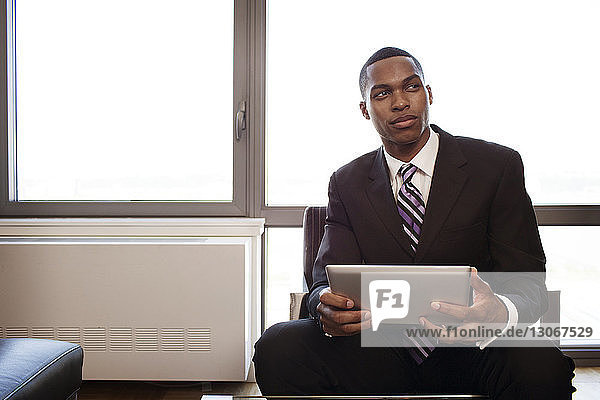 Mann mit Tablet-Computer schaut weg  während er im Büro sitzt