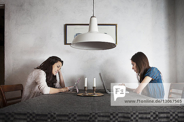 Sisters using wireless technology while sitting at dining table