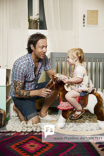 Father looking at daughter playing with rocking horse at home