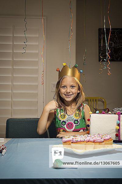 Porträt eines lächelnden Mädchens am Tisch sitzend mit Geburtstagsgeschenk und Tassenkuchen zu Hause