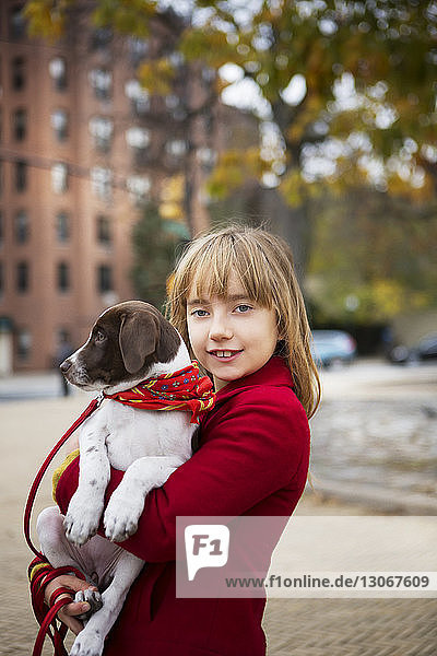 Porträt eines lächelnden Mädchens  das einen Hund trägt  während es auf einem Fußweg steht
