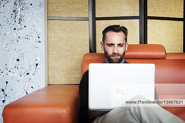 Man using laptop computer while sitting on sofa in office