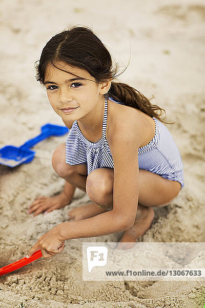 Porträt eines lächelnden Mädchens beim Spielen mit Sand am Strand