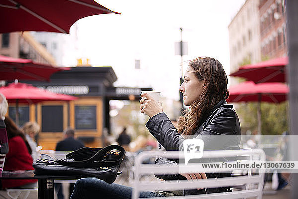 Nachdenkliche Frau hält Kaffeetasse in der Hand  während sie in einem Straßencafé in der Stadt sitzt