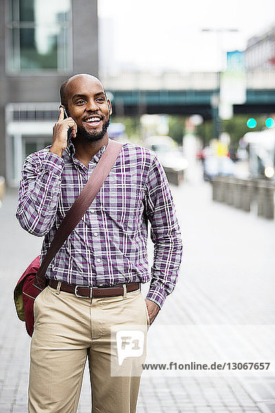Lächelnder Mann spricht mit einem Smartphone  während er in der Stadt auf der Straße geht