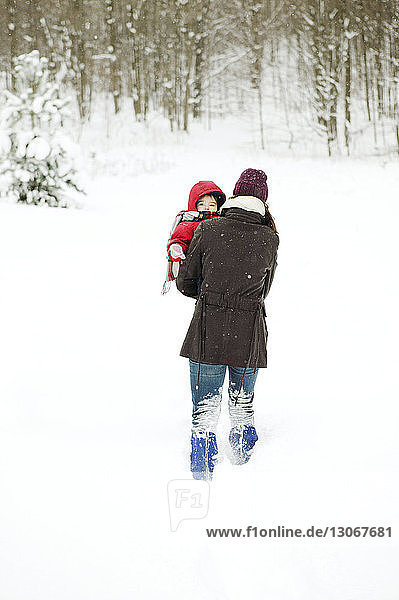 Rear view of mother carrying son while walking on snow covered field