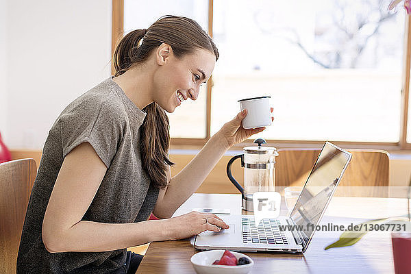 Frau benutzt Laptop  während sie zu Hause am Tisch sitzt