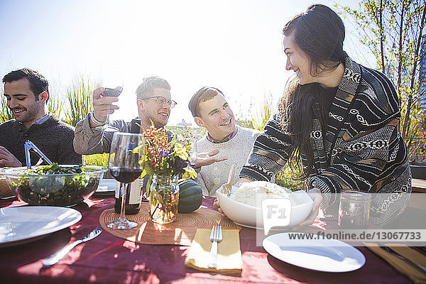Glückliche Frau serviert männlichen Freunden auf Gartenparty Essen