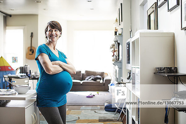 Pregnant woman with arms crossed looking away while standing at home