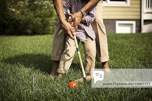 Low section of father and son playing croquet in backyard