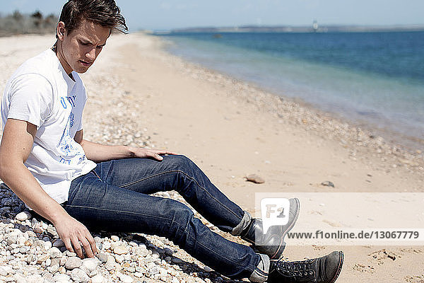 Mann schaut nach unten  während er am Strand am Ufer sitzt