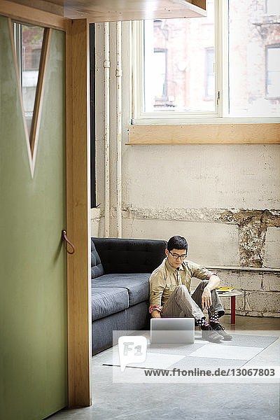Geschäftsmann benutzt Laptop-Computer  während er im Büro auf dem Boden sitzt