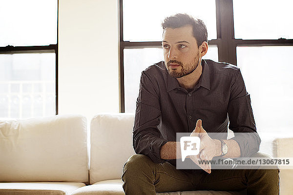 Mann schaut weg  während er zu Hause auf dem Sofa sitzt