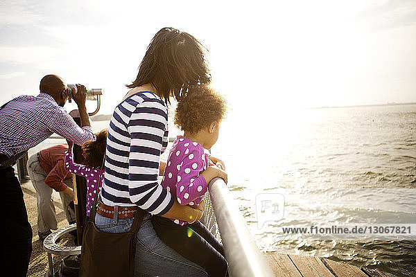 Family looking at river while standing by railing on promenade during sunny day