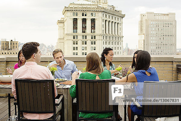 Freunde unterhalten sich beim Essen am Tisch auf der Gebäudeterrasse in der Stadt