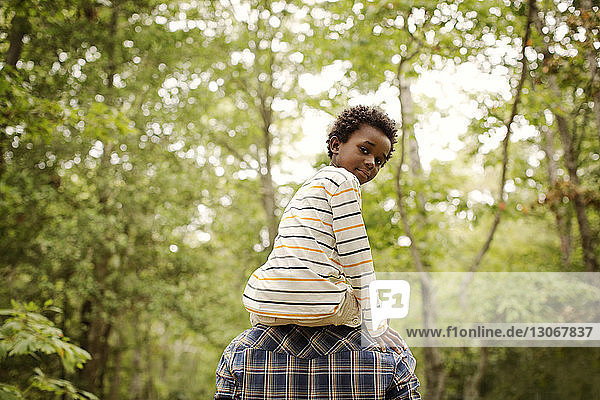 Portrait of boy being carried by father while walking in forest
