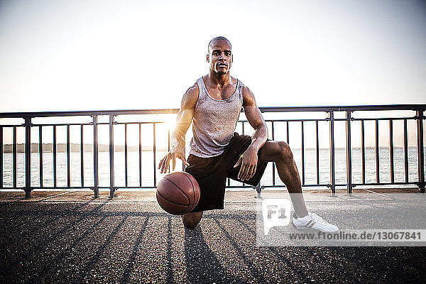 Porträt eines Sportlers  der mit Basketball auf der Brücke gegen den klaren Himmel spielt