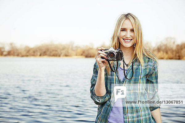 Porträt einer Frau  die am Seeufer stehend die Kamera hält