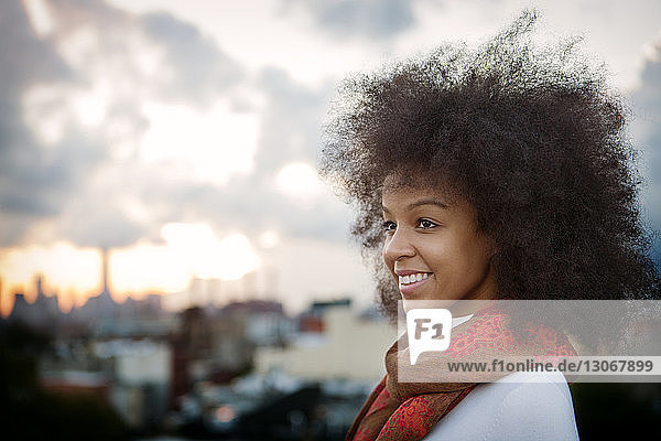 Frau mit krausem Haar schaut weg  während sie auf der Terrasse vor bewölktem Himmel steht