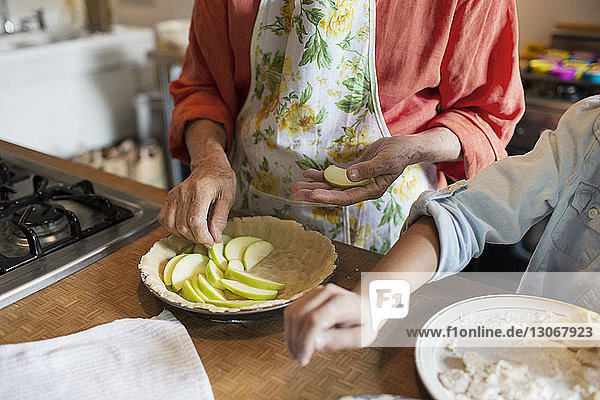 Mitschnitt einer Frau mit Enkelin beim Anrichten von Apfelschnitzen im Teller