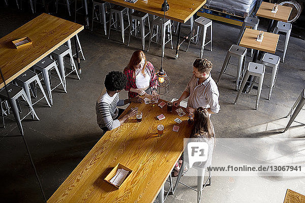 Overhead view of friends playing cards while having beer at table in brewery