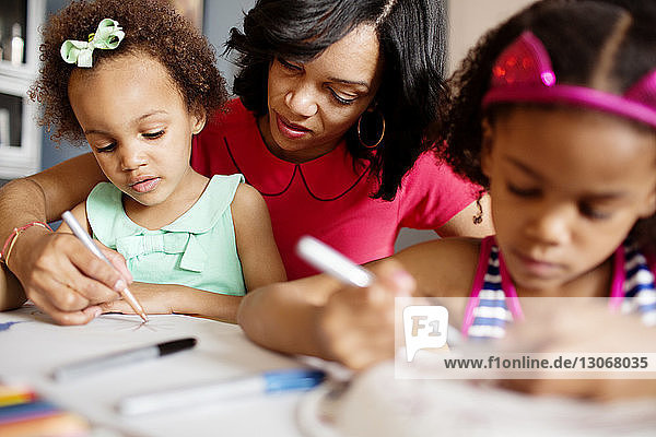 Mother assisting daughters in drawing at table