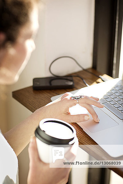 Frau hält Kaffeetasse  während sie im Café einen Laptop benutzt