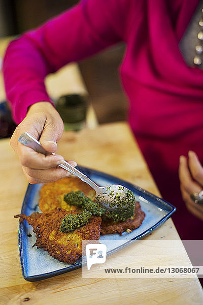 Schrägansicht einer Frau  die Essen mit grünem Chutney in einer Schale auf dem Tisch garniert