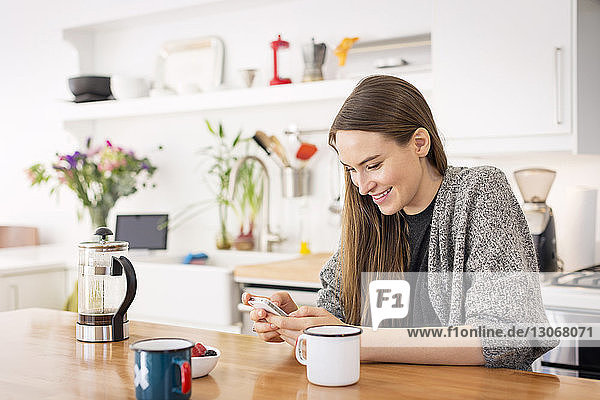 Woman using mobile phone while sitting at table in home