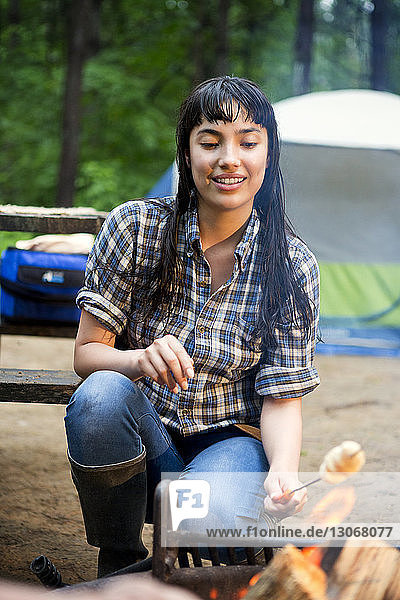 Woman roasting marshmallows while crouching by campfire in forest