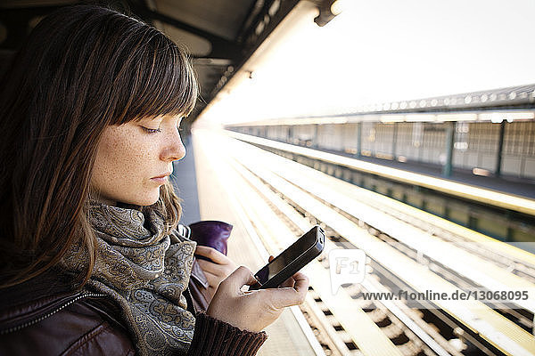Frau benutzt Smartphone am Bahnhof
