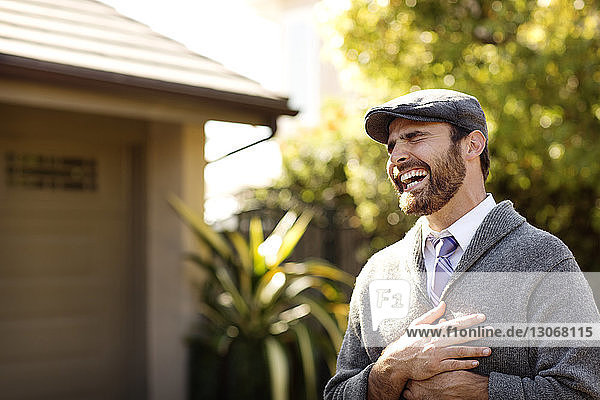 Fröhlicher Mann lacht  während er im Hinterhof steht
