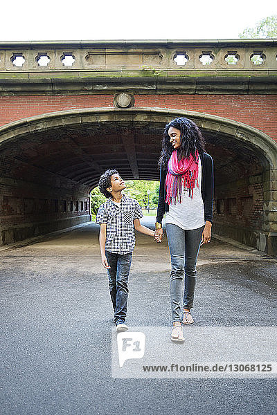 Mutter und Sohn gehen im Park gegen einen Tunnel und halten sich dabei an den Händen