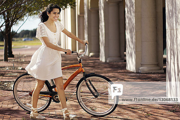 Happy teenage girl walking with bicycle on sunny day