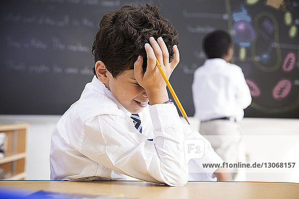 Junge mit Kopf in der Hand am Schreibtisch im Klassenzimmer sitzend