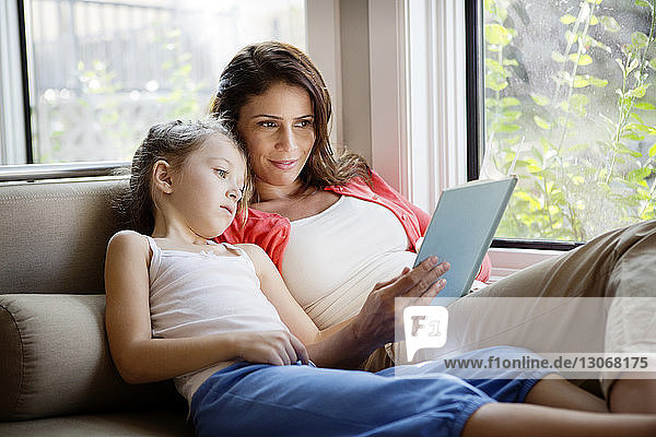 Frau unterrichtet Tochter  während sie sich zu Hause auf dem Sofa entspannt