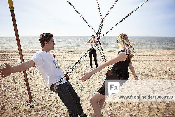 Woman photographing friends on swing at beach