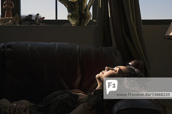 Seitenansicht einer Frau  die zu Hause am Fenster auf dem Sofa liegt