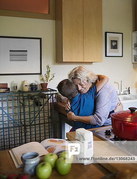 Glückliche Frau umarmt Enkel  während sie zu Hause in der Küche steht